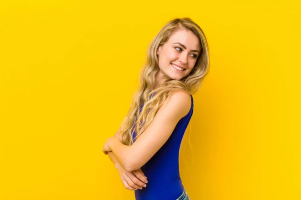 若いブロンドの女性は喜んで笑顔で 幸せを感じ 満足し リラックスし 両腕を組んで黄色の壁に反対側を見ます — ストック写真