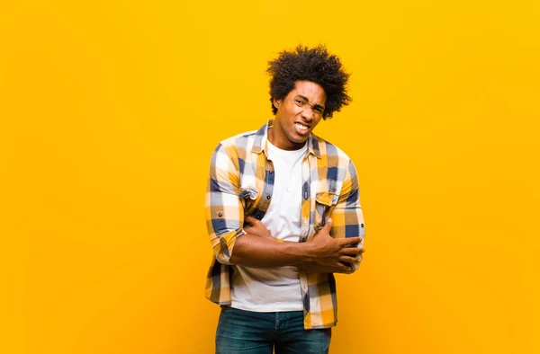 young black man feeling anxious, ill, sick and unhappy, suffering a painful stomach ache or flu against orange wall