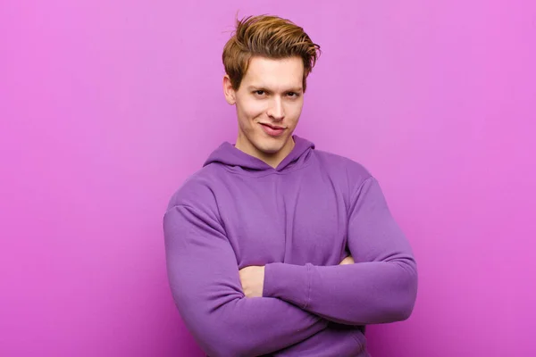 腕を組んでカメラに向かって笑っている若い赤い頭の男と幸せな 自信のある 満足そうな表情 紫色の壁に対する側面図 — ストック写真