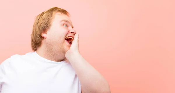 young big size man profile view, looking happy and excited, shouting and calling to copy space on the side against pink wall