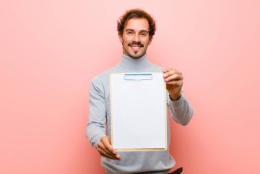 Genç ve yakışıklı bir adam pembe düz duvara karşı bir kağıt yaprağıyla