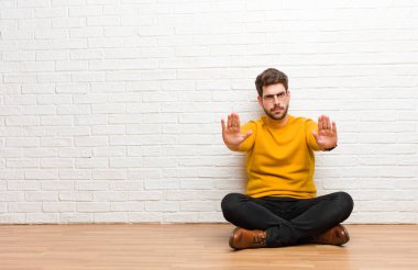 Genç yakışıklı adam tuğla duvar dokusuna karşı evde oturuyor.