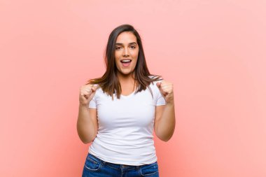 Genç ve güzel İspanyol kadın şok olmuş, heyecanlı ve mutlu hissediyor, gülüyor ve başarıyı kutluyor, vay canına! Pembe duvara yaslan