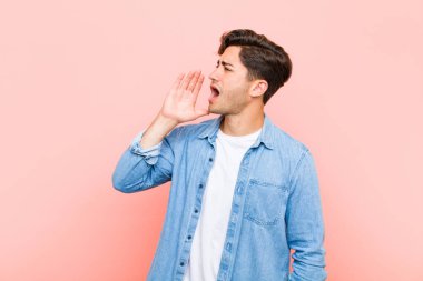 Genç yakışıklı adam öfkeyle bağırıyor kenardaki boşluğu kopyalamak için, eli ağızının yanında pembe arka planda.