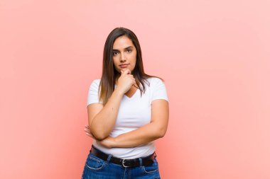 Genç, güzel, İspanyol bir kadın ciddi, kafası karışmış, kararsız ve düşünceli görünüyor. Seçenekler arasında veya pembe duvara karşı seçimler yapıyor.