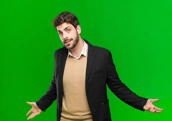 young businessman looking happy, arrogant, proud and self satisfied, feeling like a number one against green background