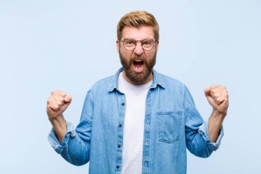 Genç, sarışın, yetişkin bir adam mutlu, şaşırmış ve gururlu hissediyor, bağırıyor ve başarıyı büyük bir gülümsemeyle kutluyor.