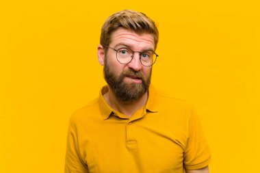 Sarışın genç adam hangi seçeneği seçeceğine karar veremiyor. Turuncu duvara karşı sorunu çözmeye çalışıyor.