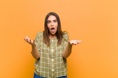 Genç ve güzel bir kadın ağzı açık ve şaşırmış, şok olmuş ve şaşırmış turuncu duvara karşı inanılmaz bir sürprizle