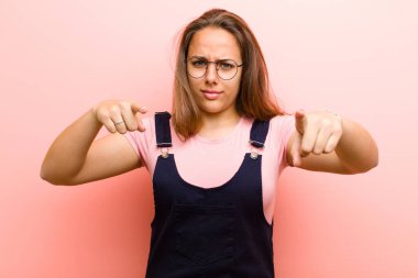 Genç bir kadın, pembe arka plana karşı görevinizi yapmanızı söyleyen, iki parmağı ve kızgın bir ifadeyle kamerayı işaret ediyor.