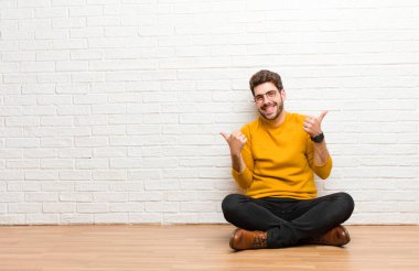 Genç yakışıklı adam tuğla duvar dokusuna karşı evde oturuyor.