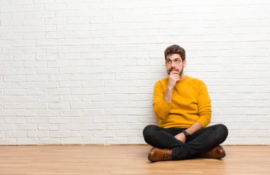 Genç yakışıklı adam tuğla duvar dokusuna karşı evde oturuyor.