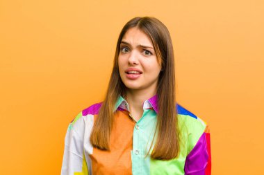 Genç, güzel bir kadın şaşkın ve şaşkın hissediyor, aptal, afallamış bir ifadeyle beklenmedik bir şeye bakıyor düz arkaplana karşı izole