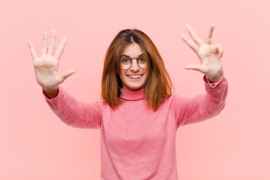 Genç, güzel bir bayan gülümsüyor ve arkadaş canlısı görünüyor. 9 ya da 9 numarayı gösteriyor. Elleri önde, pembe arka planda geriye doğru sayıyor.