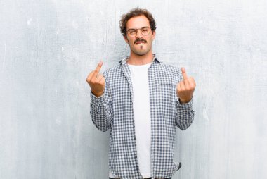 Genç yakışıklı adam kışkırtıcı, agresif ve müstehcen hissediyor, orta parmağını şıklatıyor, asi bir tavır sergiliyor, düz duvara yaslanmış.