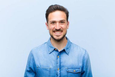 Genç yakışıklı adam mutlu ve şapşal görünüyor. Geniş, eğlenceli, kaçık bir gülüşü ve açık gözleri var.