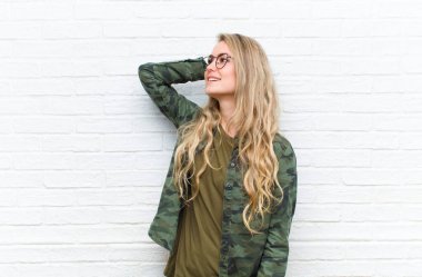 Genç sarışın kadın neşeli ve tesadüfen gülümsüyor. Olumlu, mutlu ve kendine güvenen bir bakışla duvarın arkasına bakıyor.