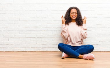 Genç Afrikalı Amerikalı siyahi kadın gülümsüyor ve endişeyle iki parmağını çapraz yapıyor. Endişeli ve iyi şanslar diliyor veya umut ediyor.