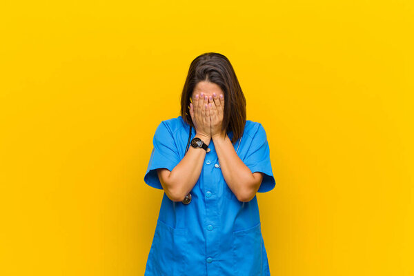 feeling sad, frustrated, nervous and depressed, covering face with both hands, crying isolated against yellow wall