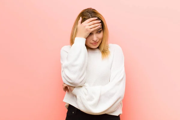 年轻漂亮的金发女人看上去紧张 羞愧或不安 双手捂住脸靠着粉红的平板墙 — 图库照片