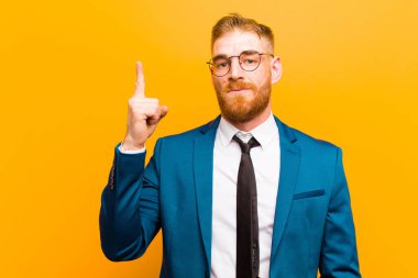 Genç kızıl saçlı işadamı, parlak bir fikri fark ettikten sonra parmağını havada tutan bir dahi gibi hissederek turuncu arka plana karşı 