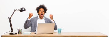 Genç siyahi iş adamı öfkeli bir ifadeyle ya da masada başarıyı kutlayan yumruklarla agresif bir şekilde bağırıyor.