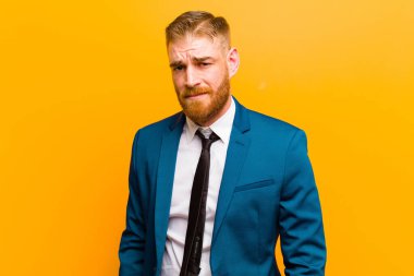 Genç kızıl saçlı iş adamı gururlu, kendinden emin, havalı, küstah ve küstah görünüyor, gülümsüyor, turuncu arka planda başarılı hissediyor.