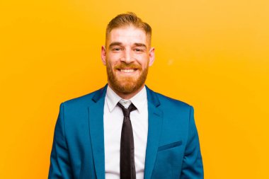young red head businessman looking happy and goofy with a broad, fun, loony smile and eyes wide open against orange background