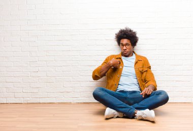 Genç siyahi adam şaşkın, şaşkın ve güvensiz hissediyor. Kendini merak edip bana mı soruyor? Evde yerde oturuyor.