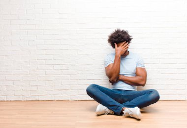 young black man looking stressed, ashamed or upset, with a headache, covering face with hand sitting on the floor at home