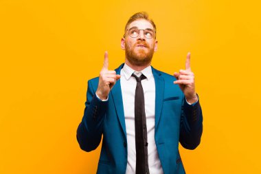 Genç kızıl saçlı işadamı hayranlık duyuyor ve ağzı açık turuncu arka planda şaşkın ve şaşkın bir bakışla yukarıya bakıyor.