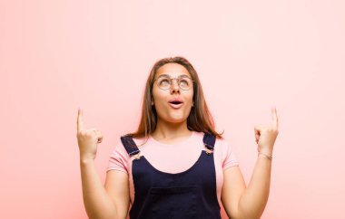 Dehşete kapılmış ve ağzı açık genç bir kadın pembe arka planda şaşkın ve şaşkın bir bakışla yukarıya bakıyor.