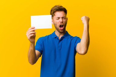 Turuncu arka planda pankart tutan genç bir adam.