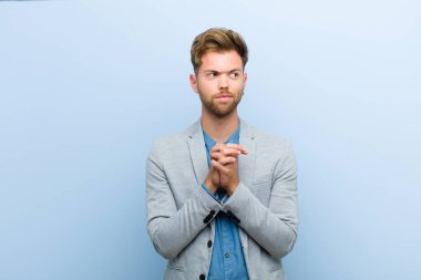 Genç işadamı gururlu, haylaz ve kibirli hissederken kötü bir plan kuruyor ya da mavi arka plana karşı bir numara düşünüyor.