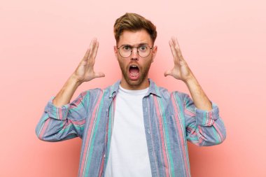 Genç adam elleri havada bağırıyor, öfkeli, sinirli, stresli ve pembe arka planda üzgün.