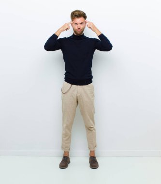 Ciddi ve konsantre görünümlü genç bir vücut adamı, beyaz arka plana karşı zorlu bir sorun hakkında beyin fırtınası yapıyor ve düşünüyor.