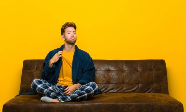 Pijama giyen genç adam kibirli, başarılı, pozitif ve gururlu görünüyor, kendini işaret ediyor. Kanepede oturuyor.