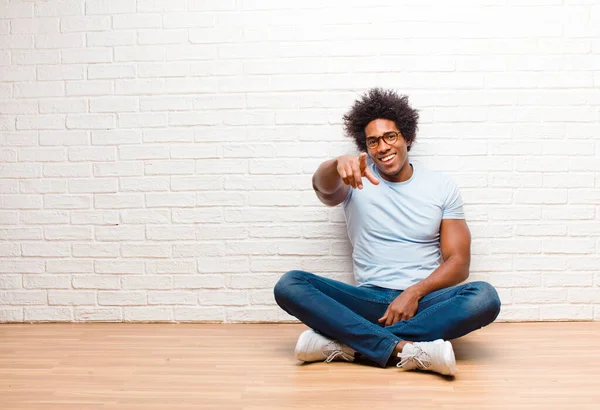 young black man pointing at camera with a satisfied, confident, friendly smile, choosing you sitting on the floor at home