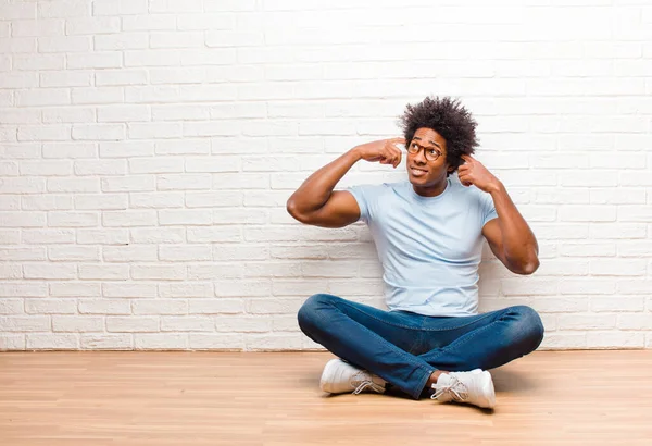 若い黒人男性は混乱や疑問を感じ アイデアに集中し 一生懸命考え 家の床に座っている空間をコピーしようとしています — ストック写真