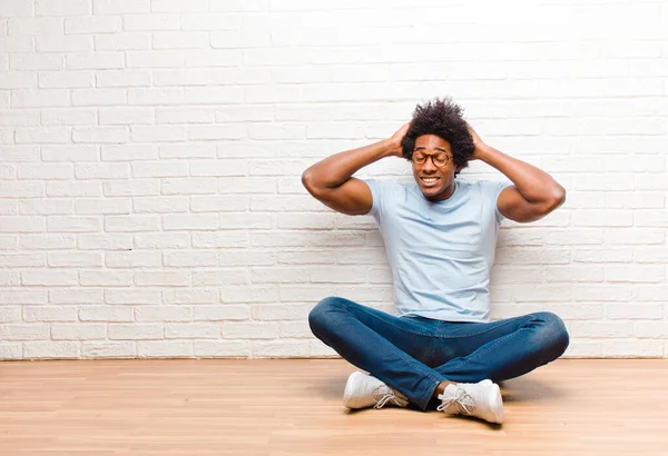 若い黒人男性はストレスを感じ 心配し 不安や恐怖を感じ 手を頭の上に置き 家の床に座っている間に誤ってパニックに陥りました — ストック写真