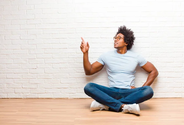 若い黒人男性が立ってコピースペースを指差して家の床に座って — ストック写真