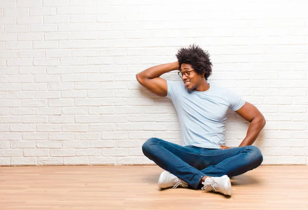 young black man thinking or doubting, scratching head, feeling puzzled and confused, back or rear view sitting on the floor at home