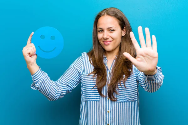 Jonge vrouw met een smiley gezicht tegen blauwe achtergrond — Stockfoto