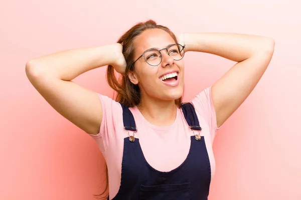 young  woman smiling and feeling relaxed, satisfied and carefree, laughing positively and chilling against pink background