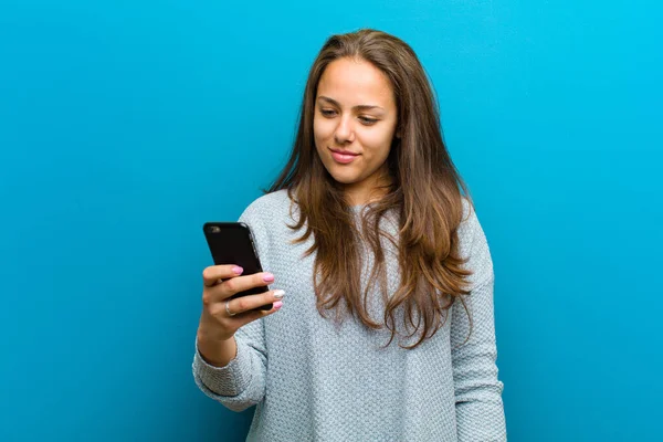 Ung kvinna med mobiltelefon mot blå bakgrund — Stockfoto