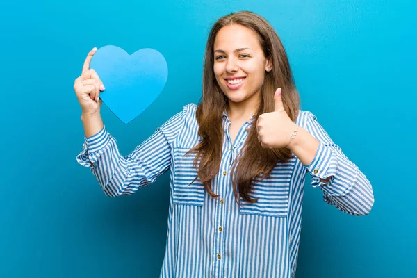 Jovem com uma forma de coração contra fundo azul — Fotografia de Stock