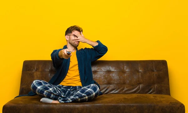 young man wearing pajamas and sitting on a sofa with a remote control