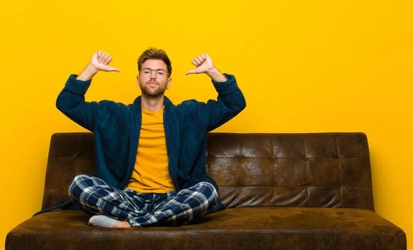 young man wearing pajamas feeling proud, arrogant and confident, looking satisfied and successful, pointing to self . sitting on a sofa