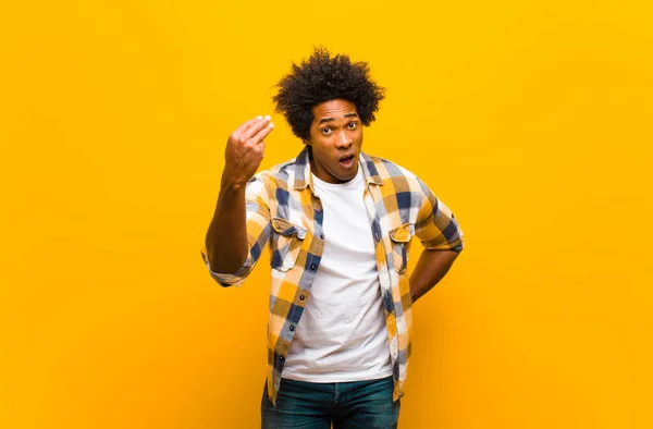 年轻的黑人男人在做花言巧语或金钱手势 让你还债 相对于橙色墙 — 图库照片