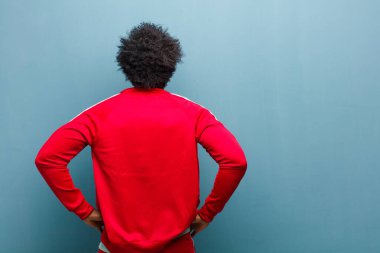 Genç siyah sporcu kafası karışık ya da dolu hissediyor ya da şüphe ve sorular, merak ediyor, elleri kalçasında, dikiz aynasıyla grunge duvarına bakıyor